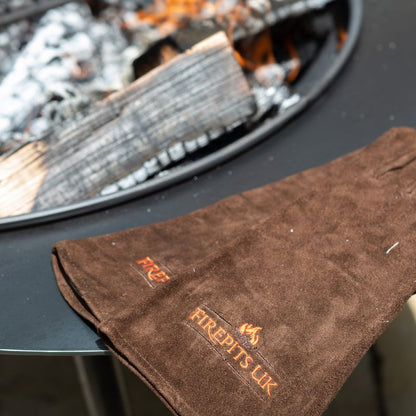 Firepits UK Fire Pit BBQ Gloves in brown beside a fire pit